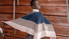 a woman standing in front of a wooden wall with a blue and white blanket on her shoulders