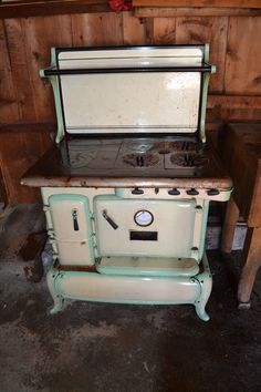 an old fashioned stove sitting in a room next to a wooden table and wall with wood paneling on the walls