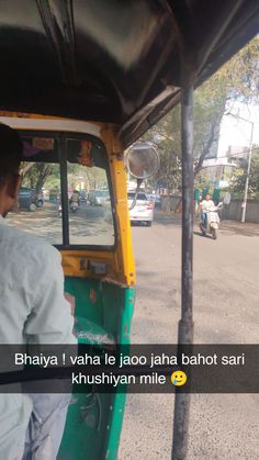 a man riding on the back of a green and yellow truck down a street next to a sidewalk