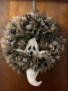 a wreath decorated with black and white striped decorations on a wooden door hanger that has a ghost's head hanging from it