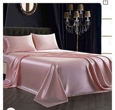 a bed covered in pink sheets and pillows next to a window with chandelier