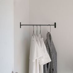 three white shirts hanging on a rail next to a pair of gray shoes and a coat rack