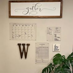 a wall with calendars on it and a wooden sign hanging from the wall next to a potted plant