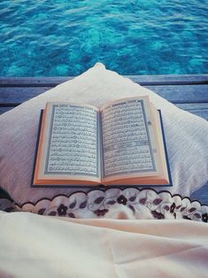 an open book sitting on top of a bed next to a pool with blue water