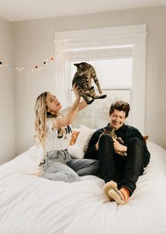 a man and woman sitting on top of a bed with a cat in their hands