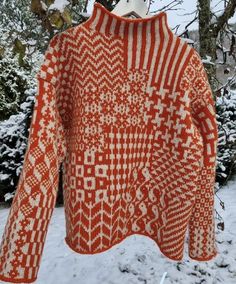 an orange and white knitted sweater hanging on a clothes rack in the snow with trees behind it