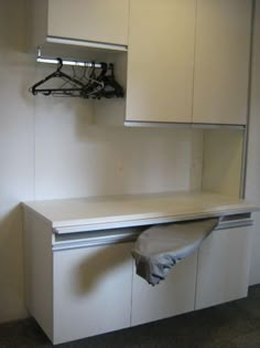 an empty room with white cabinets and clothes hanging on the wall above it is a towel rack