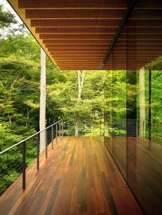 a wooden deck with glass railings and trees in the backgroung area