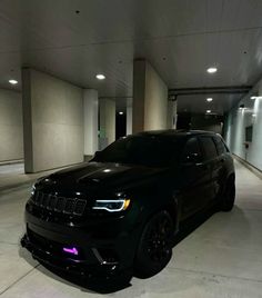 a black jeep is parked in an empty parking garage with purple lights on the side