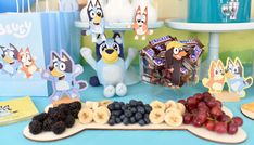 a table topped with fruit and snacks on top of a blue tablecloth covered in cartoon characters