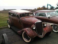 two old cars parked next to each other in a parking lot with an excavator behind them