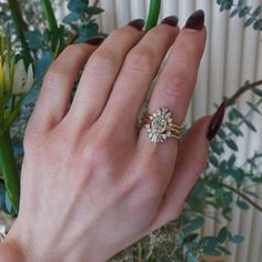 a woman's hand with two rings on her fingers and flowers in the background