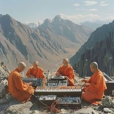 four monks are sitting on top of a mountain playing an electronic device with mountains in the background