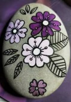 a rock with flowers painted on it sitting on a purple surface next to other pictures