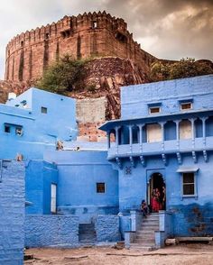 blue buildings in india with a castle on the hill behind them and people standing at the entrance