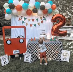 a little boy standing in front of a table with balloons on it and a sign that says 2