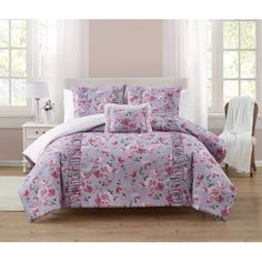 a bed in a room with pink flowers on the comforter and white curtains,