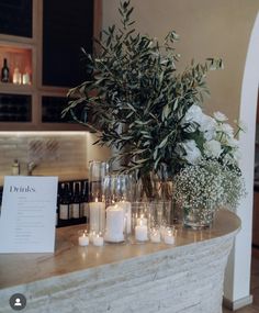 candles are lined up on a counter with flowers and wine bottles