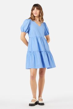 Blue mini smock dress, with a sweet v neckline. Featuring a two tier skirt, short puff sleeves & made of a cotton viscose blend. - slip on this easy relaxed style smock- soft v neckline with a sweet puff sleeve- mini length featuring a tiered skirt with exposed ruffle- handy side pocket- elastic hem on sleeve- side ties to cinch in at waist- made of a smooth viscose cotton blend- available in cornflower Product Code: PGFY141 Summer Puff Sleeve V-neck Dress With Ruffle Hem, Blue V-neck Puff Sleeve Dress For Spring, Blue V-neck Tiered Dress With Ruffle Hem, Spring Cotton V-neck Dress With Short Sleeves, Short Sleeve Cotton V-neck Dress For Spring, Cotton Mini Tiered Dress For Brunch, Cotton Mini Length Tiered Dress For Brunch, Blue Tiered Mini Dress For Spring, Blue Tiered Skirt Mini Dress For Spring