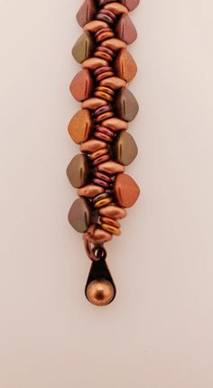 a beaded necklace is hanging from a hook on a white wall with an orange and brown bead