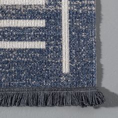 a blue and white rug with fringes hanging on the wall next to a gray wall