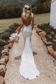 a woman in a white wedding dress walking down a path with her back to the camera