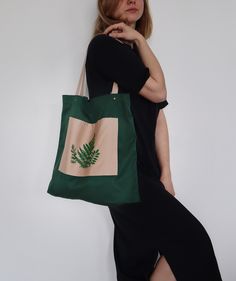 a woman in black dress holding a green and beige bag with fern leaves on it