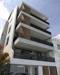 a black car parked in front of a tall white building with balconies on the second floor