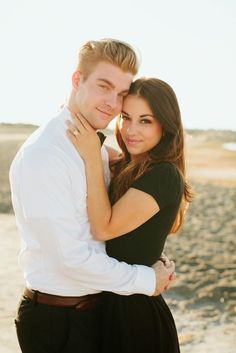 a young man and woman embracing each other on the beach in front of the ocean