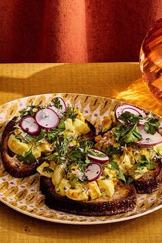 an open face sandwich on a plate next to a glass of wine and a vase