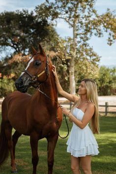 a beautiful young woman petting a brown horse