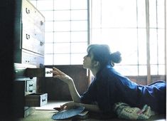 a woman sitting on the floor in front of an open drawer holding a paper fan