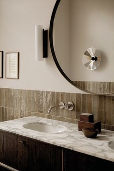 a bathroom sink sitting under a round mirror next to a wall mounted faucet