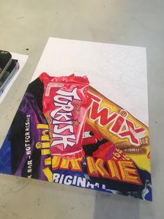 a piece of paper that has some kind of candy wrapper on it, next to two markers and pencils