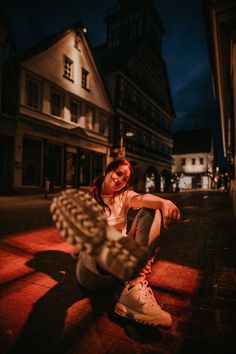 a young woman sitting on the ground in front of a building at night with her arms crossed