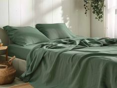 a bed with green sheets and pillows in a room next to a basket on the floor