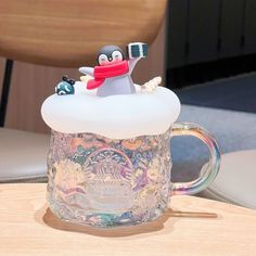 there is a glass mug with a penguin in it sitting on top of a table