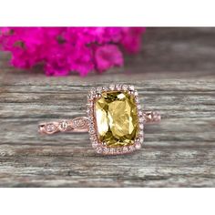 a yellow and white diamond ring on top of a wooden table with pink flowers in the background