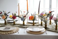 a table topped with plates and vases filled with flowers next to candles on top of a table