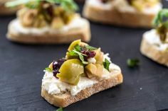 small pieces of bread with olives, cheese and herbs on them sitting on a black surface