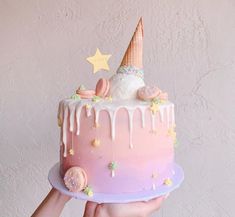 a hand holding a cake with icing and stars on it, in front of a wall