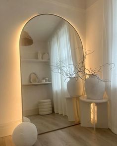 a white vase sitting on top of a wooden floor next to a large round mirror