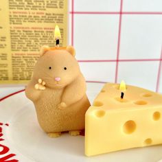 a small toy hamster sitting next to a piece of cheese on a plate with a red and white checkered wall behind it