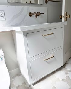 a white bathroom with marble counter tops and gold handles on the drawers next to the toilet