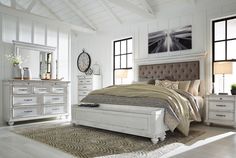 a bedroom with white furniture and large windows in the room, including a bed that has an upholstered headboard