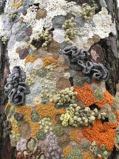 crocheted flowers and leaves are on the bark of a large tree trunk, which is covered in multicolored yarn