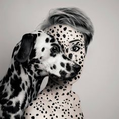 a woman with black and white polka dots on her face is hugging a dalmatian dog