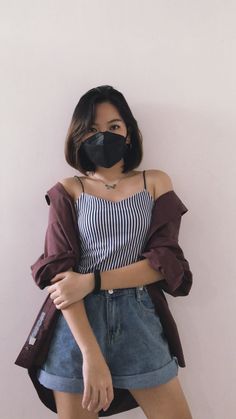 a woman wearing a black mask standing in front of a white wall