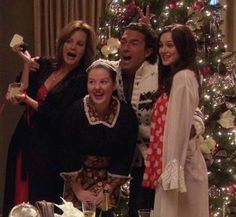 three women and one man standing in front of a christmas tree