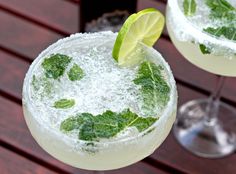 two margaritas with lime and mint garnish sit on a table